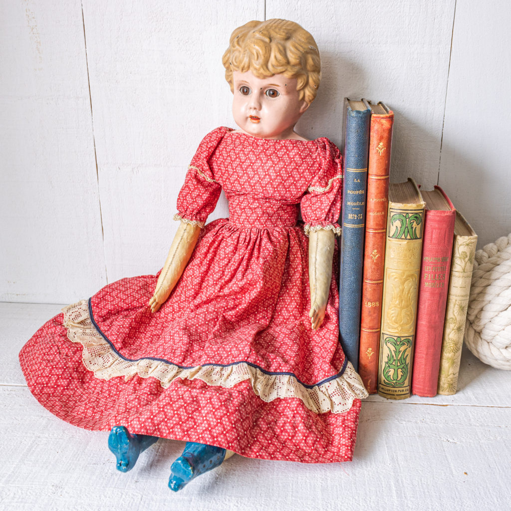 A cloth doll with a Minerva metal head in a red dress with blue boots sitting beisde some antique books