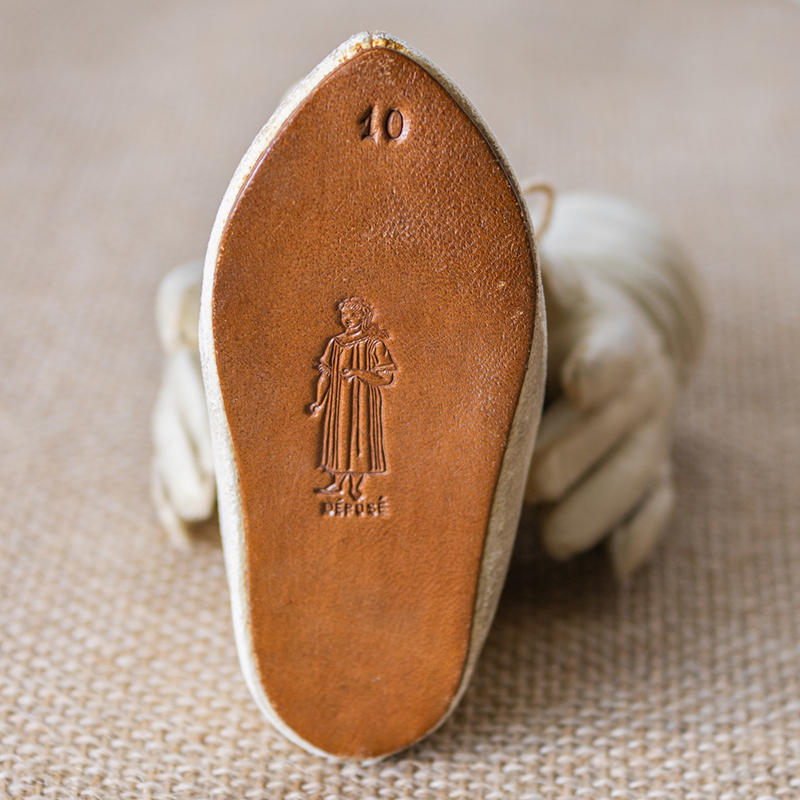 The sole of an antique French white leather doll shoe from doll sold in 1912 by Eugene Alart with the trademark of woman in chemise barefoot